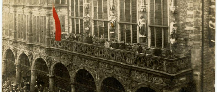 Ausrufung der Machtübernahme durch den Arbeiter-und-Soldaten-Rat am 15. November 1918 vom Balkon des Bremer Rathauses. (Foto: [url=https://de.wikipedia.org/wiki/Bremer_R%C3%A4terepublik#/media/File:Rathaus_Bremen_15111918.jpg]Barth - Staatsarchiv Bremen[/url])