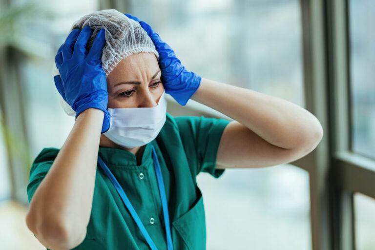 340302b distraught nurse wearing protective workwear while holding her head pain medical clinic - Genauso falsch wie überall - Krankenpflege - Krankenpflege