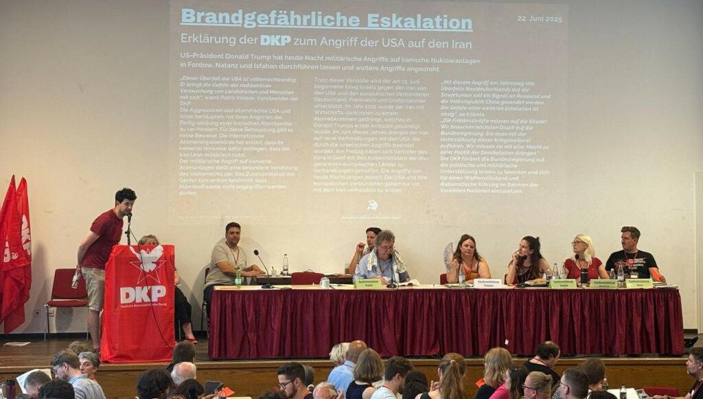 DKP und UZ aktuell zum US-Überfall auf den Iran - - Die Erklärung der DKP zum US-Angriff auf den Iran wurde an die Wand hinter dem Präsidium des Parteitages geworfen. Foto: UZ