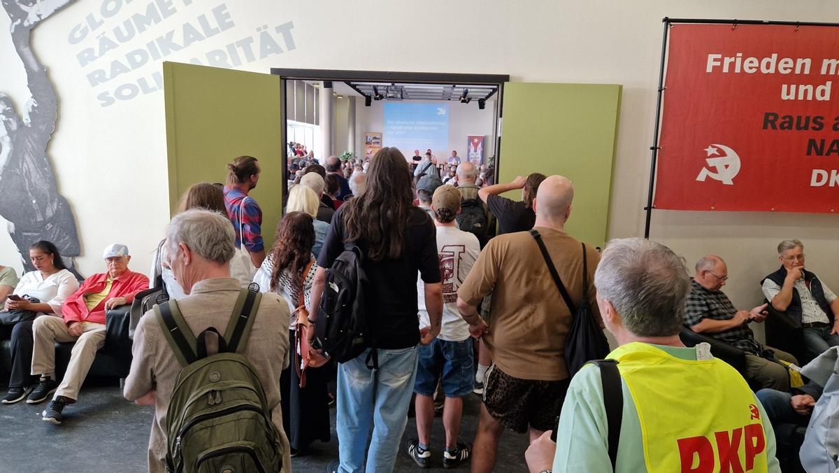 saal voll - Frohen Mutes durch finstere Zeiten - An­drea Hornung, Ana Prestes, André Scheer, Anne Rieger, Banda Bassotti, Benedikt Kolbe, Berlin, Björn Blach, DKP, Egon Krenz, Erich Schaffner, Frauke Pietsch, Friedensfest, Gina Pietsch, Hartmut König, ICAP, Jörg Kronauer, Jutta Kausch-Henken, Lühr Henken, Mark Ellmann, Melina Deymann, Miguel Torres Tesoro, Naser El-Mokdad, Nonni Morisse, Patrik Köbele, PCC, Rainer Perschewski, Renate Koppe, SDAJ, Sergej Netschajew, Sevim Dağdelen, Sigaro, Sun Shouliang, Tatjana Sambale, Tawfik Lababidi, Timo Reuter, Ulrike Eifler, UZ-Friedenstage 2026, Wera Richter - Hintergrund
